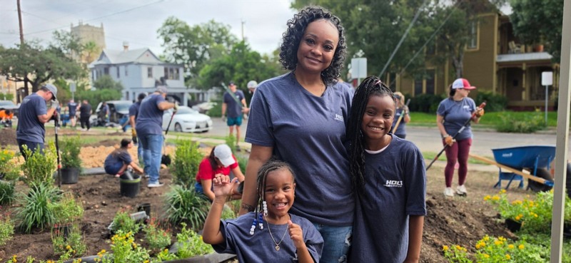 A HOLT volunteer and her children smile in front of freshly planted landscaping