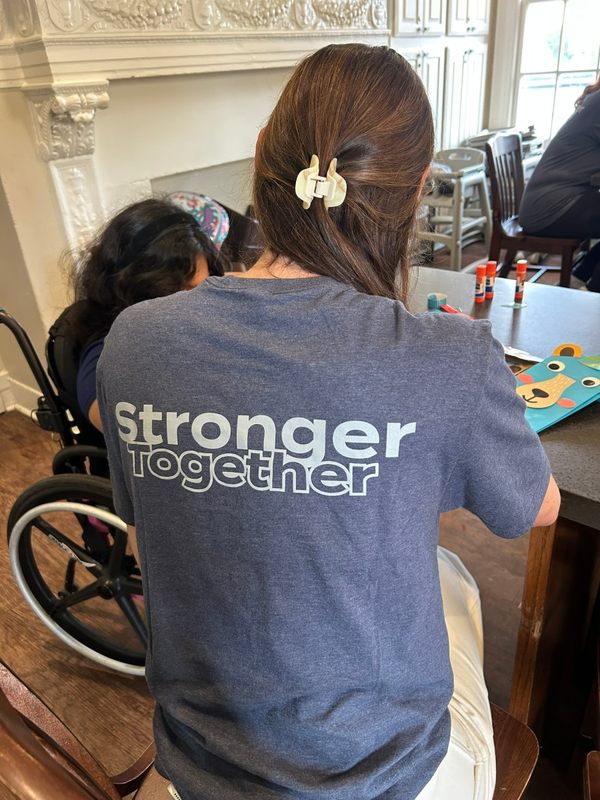 A volunteer in a Stronger Together shirt prepares crafts at a classroom table